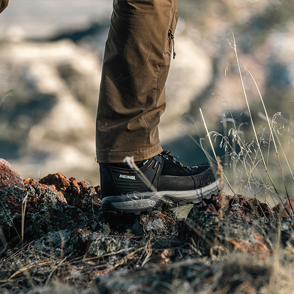 Meindl Alpine 1.5 light hiking boot – Black  Suede Leather Gore-Tex Hiking Shoe Worn on Rocky Ridge With Blurred Boulder and Grass Background
