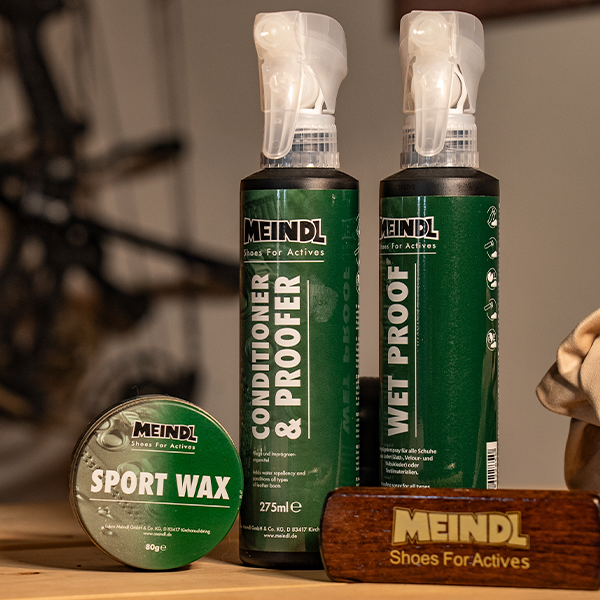 Meindl Boot Care Products – Meindl Sport Wax, Conditioner and Proofer Spray, and Wet Proof Spray Displayed on a Wooden Surface With a Meindl Branded Brush
