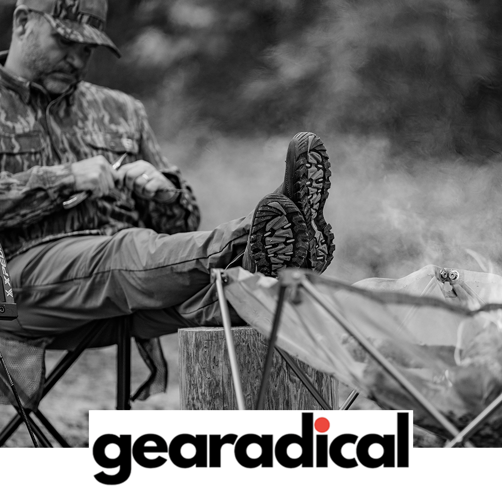 Meindl Comfort Fit Camp Moc Slip-On – As Featured in Gearadical – Leather Moccasin Camp Shoe Worn by Bowhunter in Camouflage Relaxing at Campfire With Feet Up on Log Showing Vibram Outsole