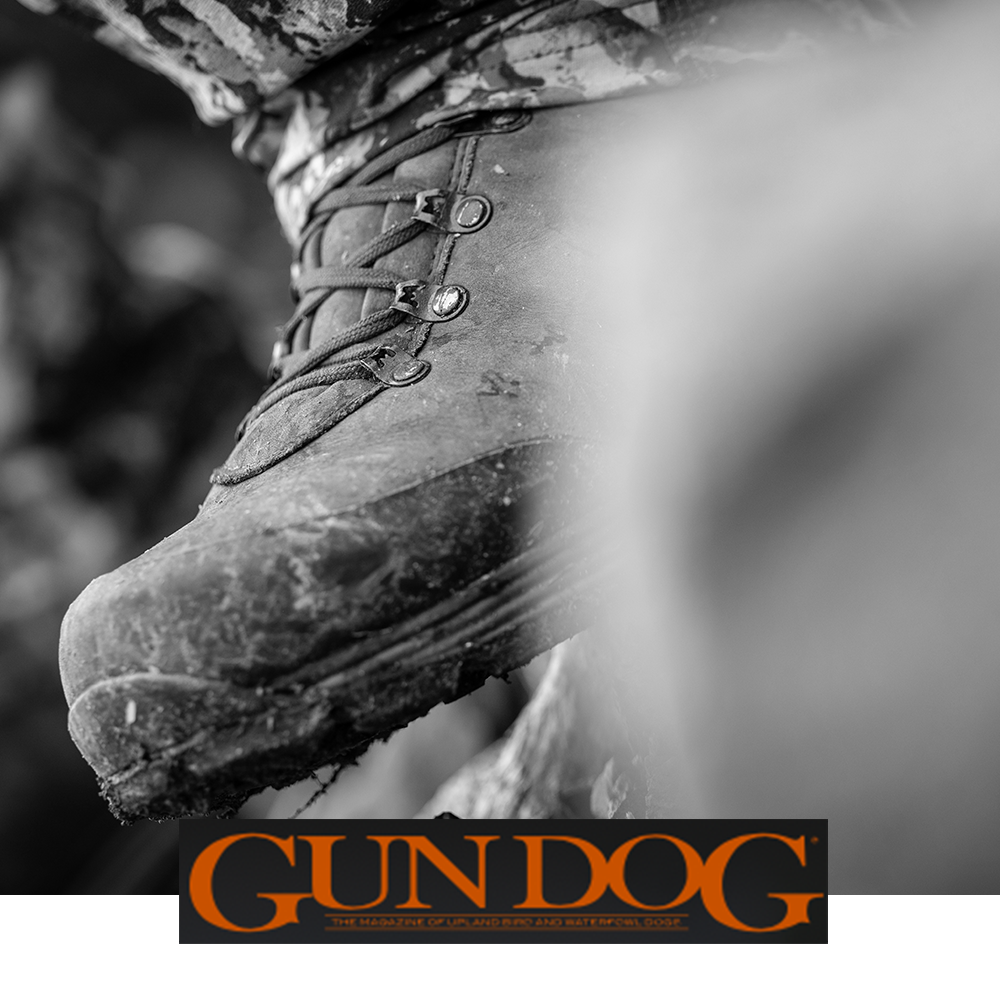 Meindl Comfort Fit Hunter Uninsulated – As Featured in Gun Dog Magazine – Uninsulated Leather Hunting Boot Worn by Upland Hunter in Camouflage on Muddy Rocky Terrain With Hunting Dog Visible in Background