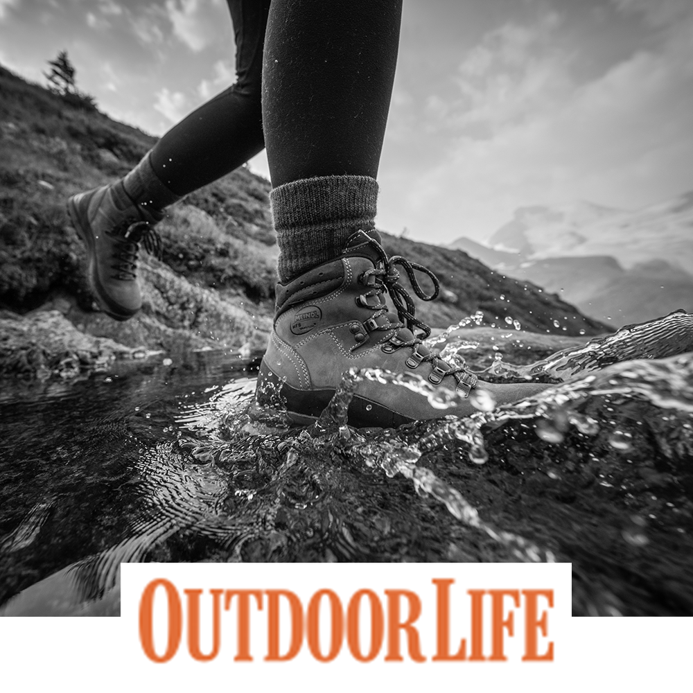 Meindl Lady MFS Vakuum Hiker – As Featured in Outdoor Life Magazine – Women's MFS Vakuum Custom-Fit Hiking Boot Worn by Female Hiker Crossing Rocky Alpine Stream With Mountains in Background