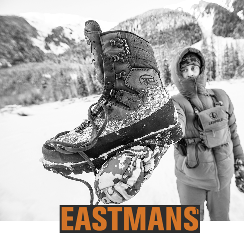 Meindl MFS Glockner GTX – As Featured in Eastmans' Hunting Journal – Gore-Tex Alpine Hunting Boot Held Up and Covered in Snow Showing DiGAfix Lacing, MFS System Badge, and Gore-Tex Label With Hunter and Snow-Covered Mountains in Background