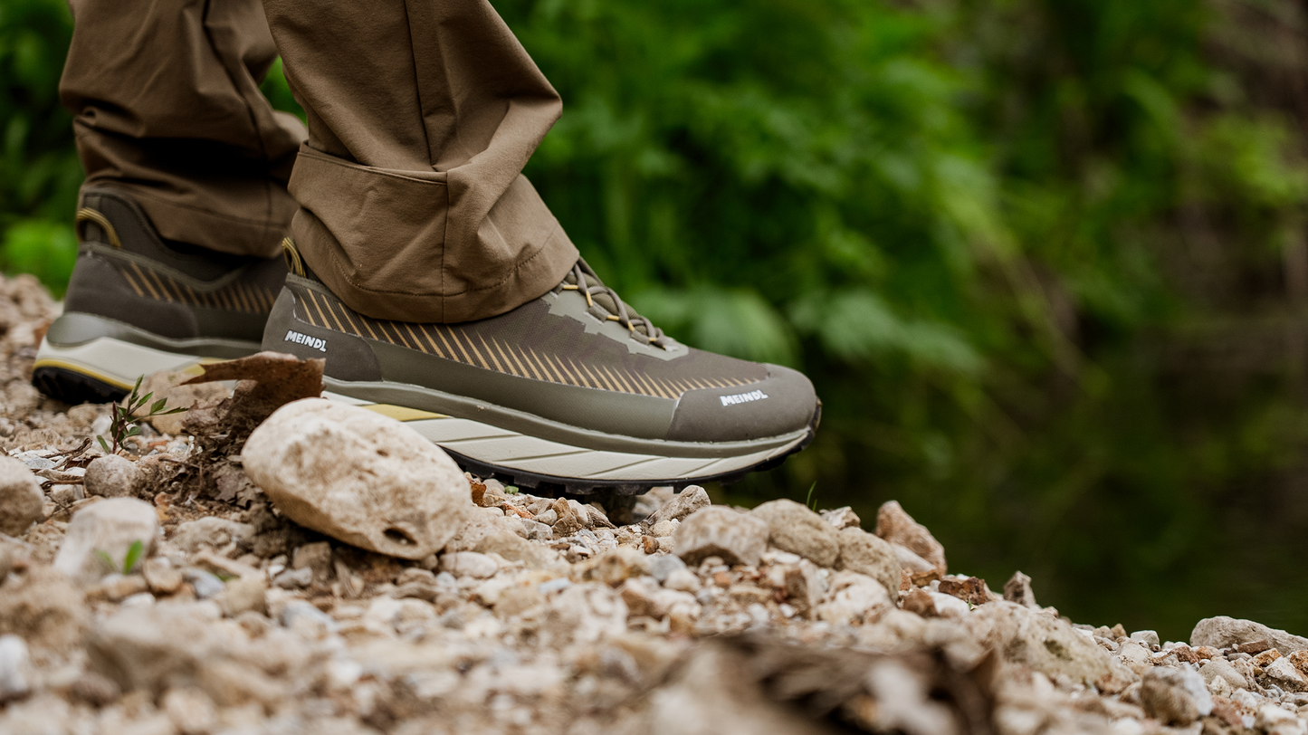 Meindl Eldora GTX Trail Runner – Olive Green and Gold Low-Cut Gore-Tex Trail Running Shoe Worn on Rocky Gravel Trail With Green Forest Background