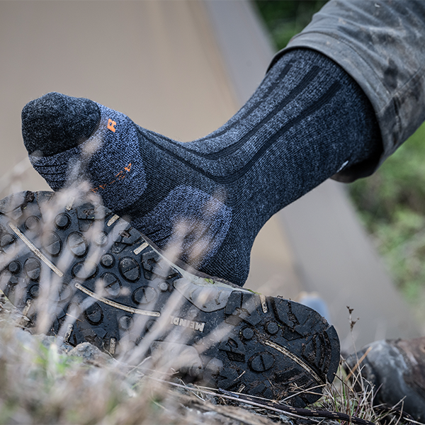 Meindl Hiking Socks – Blue and Orange Merino Wool Boot Sock Worn on Foot Stepping Over Rocky Ground With Meindl Boot Outsole Visible Beneath